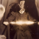 Physical medium demonstrating spiritual energy, with visible beams of light between their hands, while an observer watches closely.