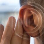 Close-up image of a human ear with digital sound waves illustrated around it, symbolizing auditory perception or the detection of subtle sounds.
